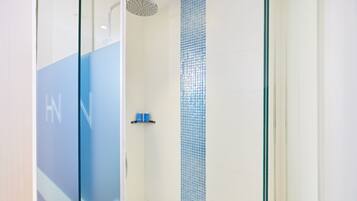 A modern shower with a glass door, a blue-tiled wall, and a shelf with toiletries.