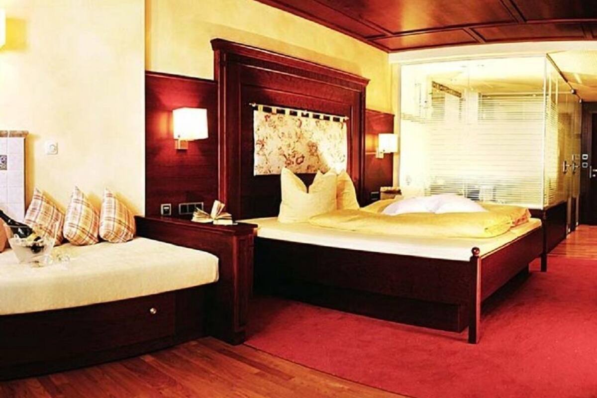 Une chambre d’hôtel avec un grand lit, des tables de chevet, une petite table, une lampe et une fenêtre avec des stores.
