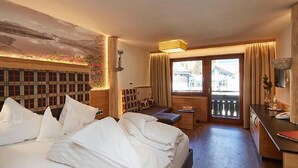 A hotel room with a bed, a desk, a bench, and a view of the outside. - Alpenrose - Wellnessresort (Elbigenalp)