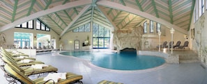 En indendørs swimmingpool med liggestole, klippeformation og et hvælvet loft med grønne bjælker.