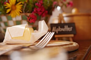 A butter dish with a knife on a wooden board, a sign that reads "Butter," and a vase with flowers in the background. - Wellnesshotel Warther Hof (Warth)