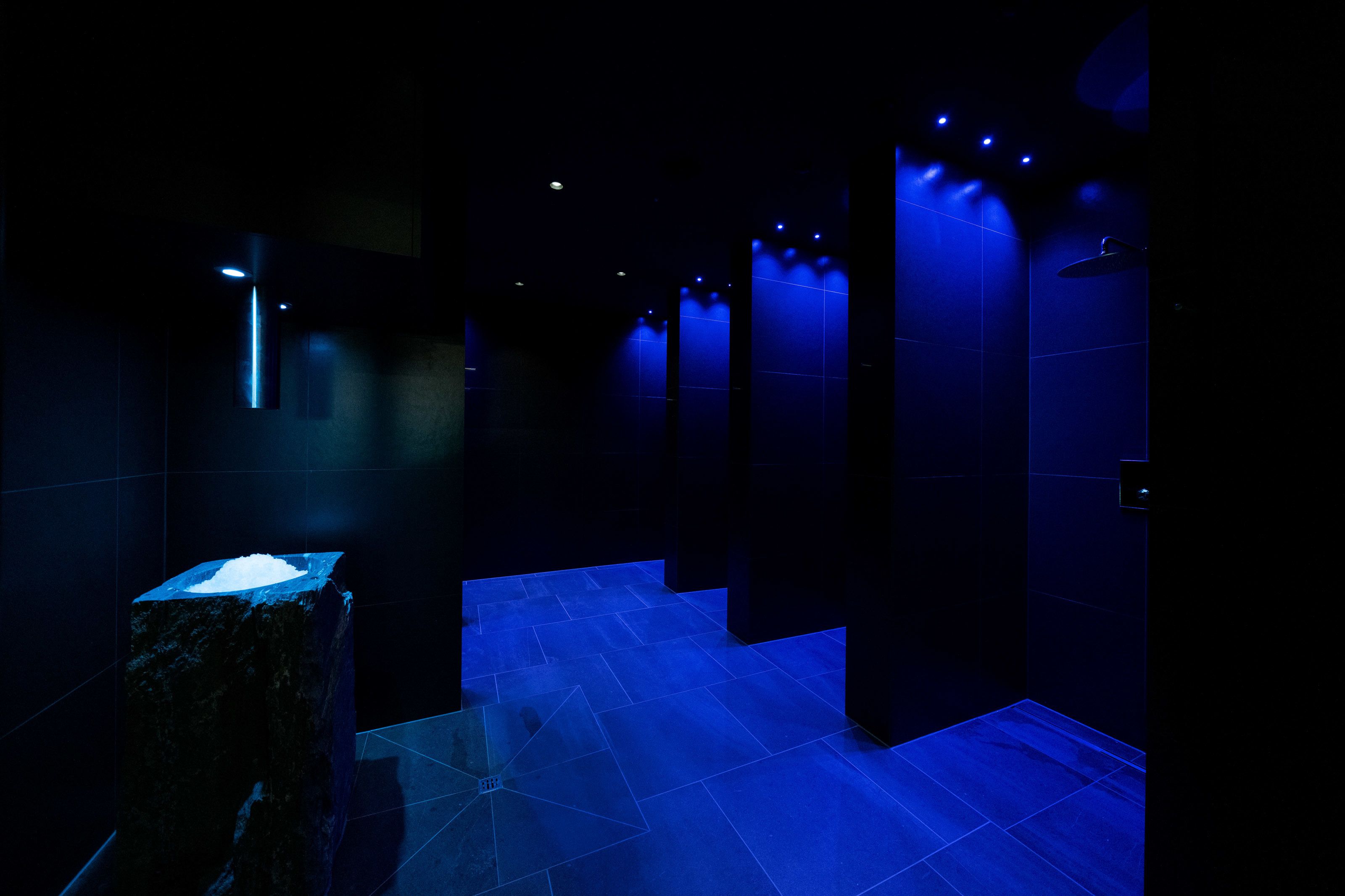 A dimly lit hallway with blue ambient lighting, tiled walls, and a stone pedestal.