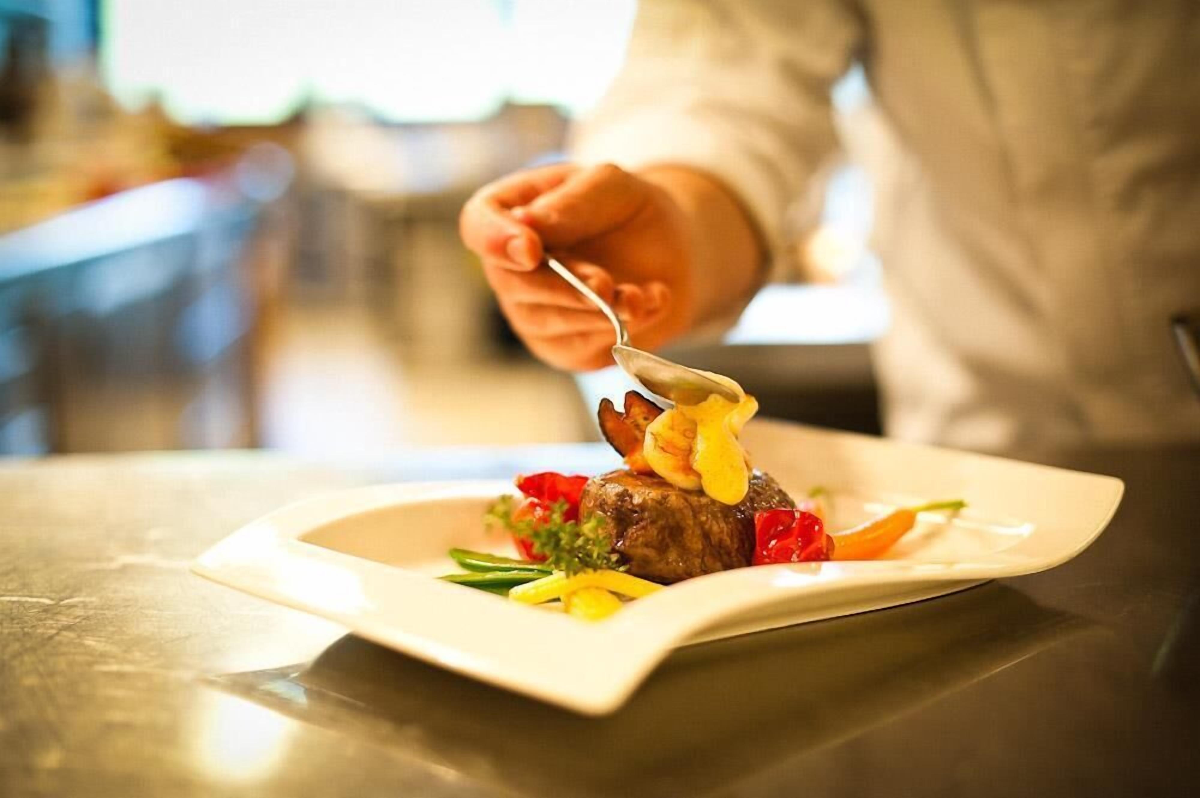 A person serving a steak with vegetables on a white plate.