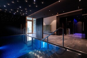 Una piscina interior moderna con barrera de vidrio, suelo de baldosas de piedra y diseño de techo que simula un cielo estrellado.