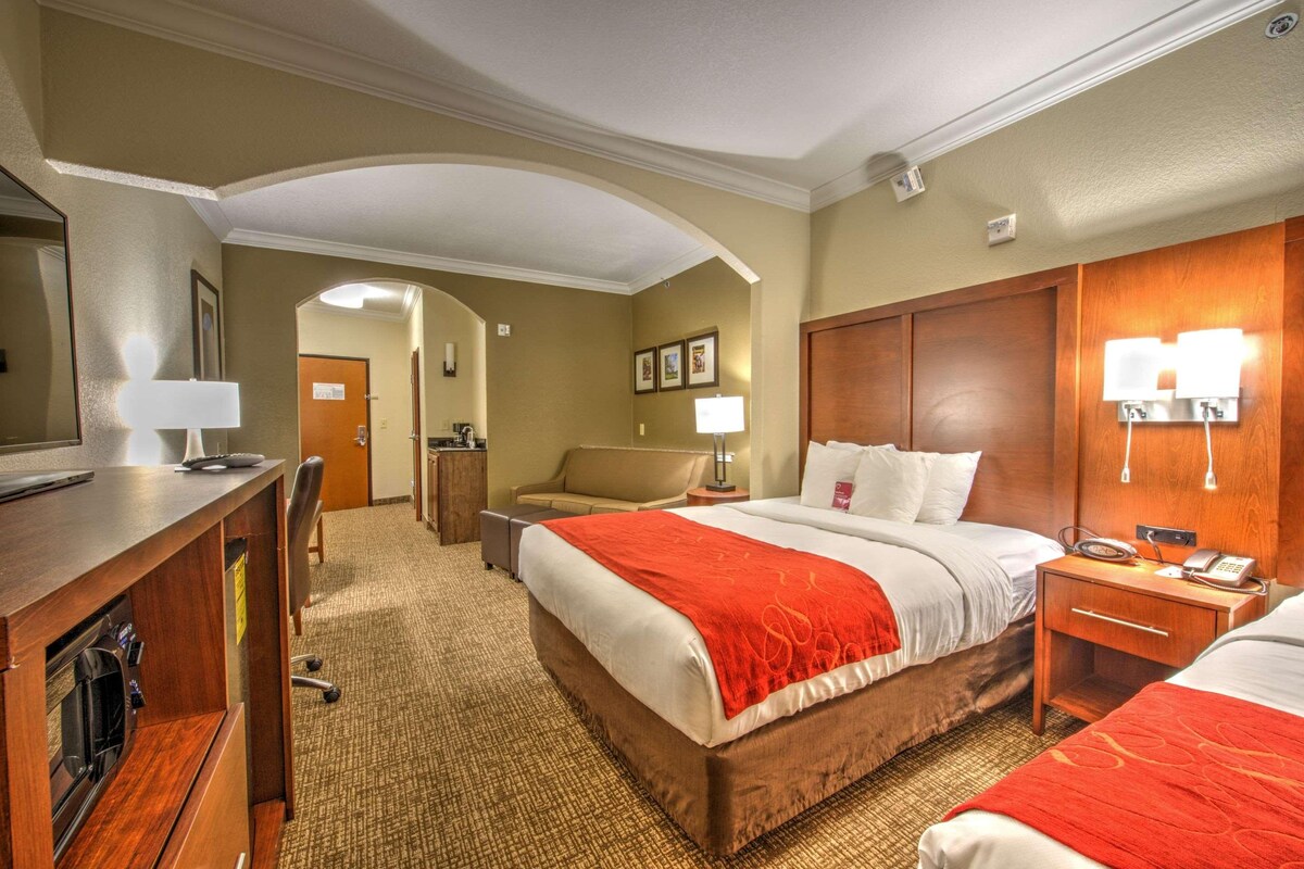 A hotel room with a large bed, a desk, a chair, a nightstand, and a lamp.
