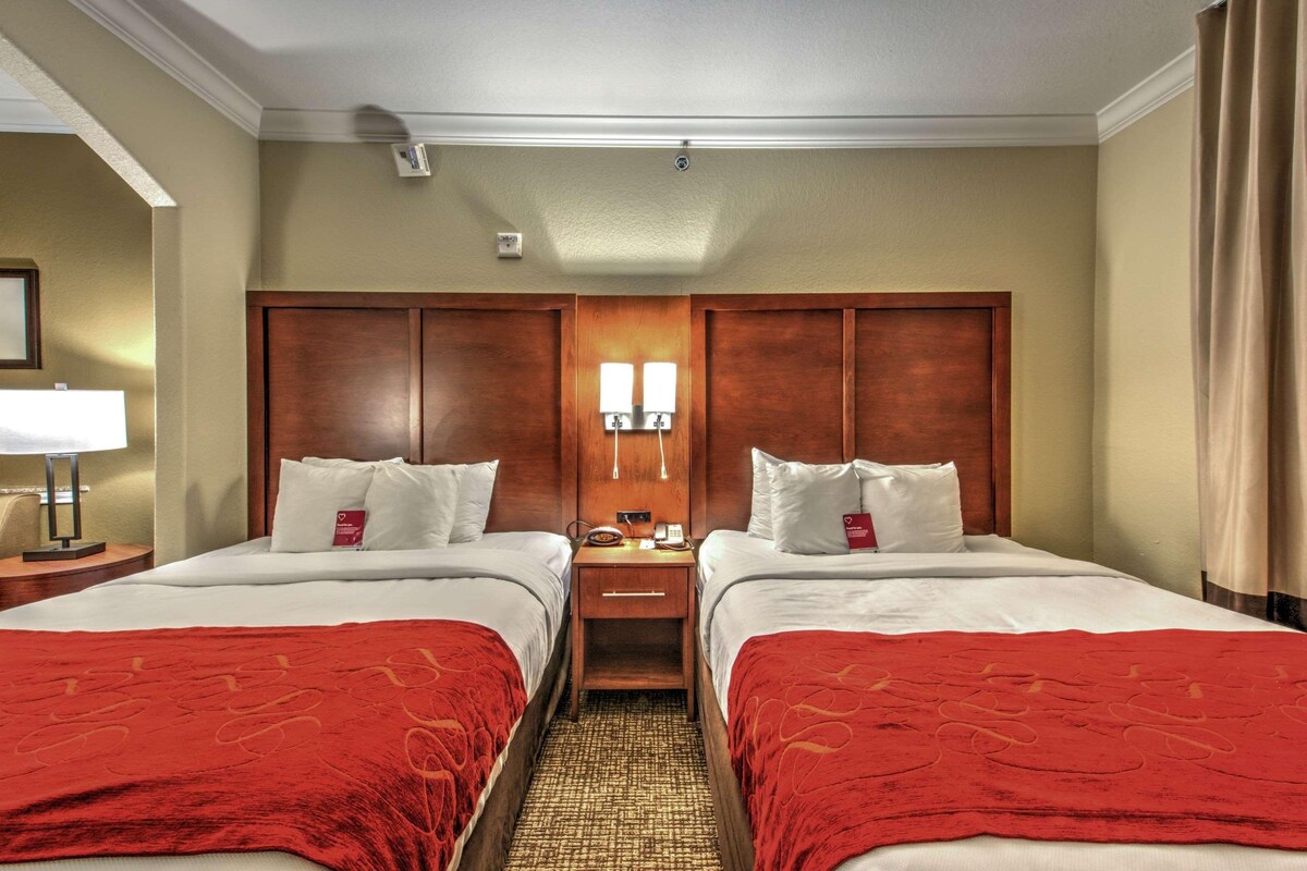 A hotel room with two beds, a wooden headboard, bedside lamps, and a red throw blanket.