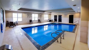 Una piscina interior con las normas de la piscina claramente expuestas, una silla de salvavidas y una zona de estar con mesas y sillas.