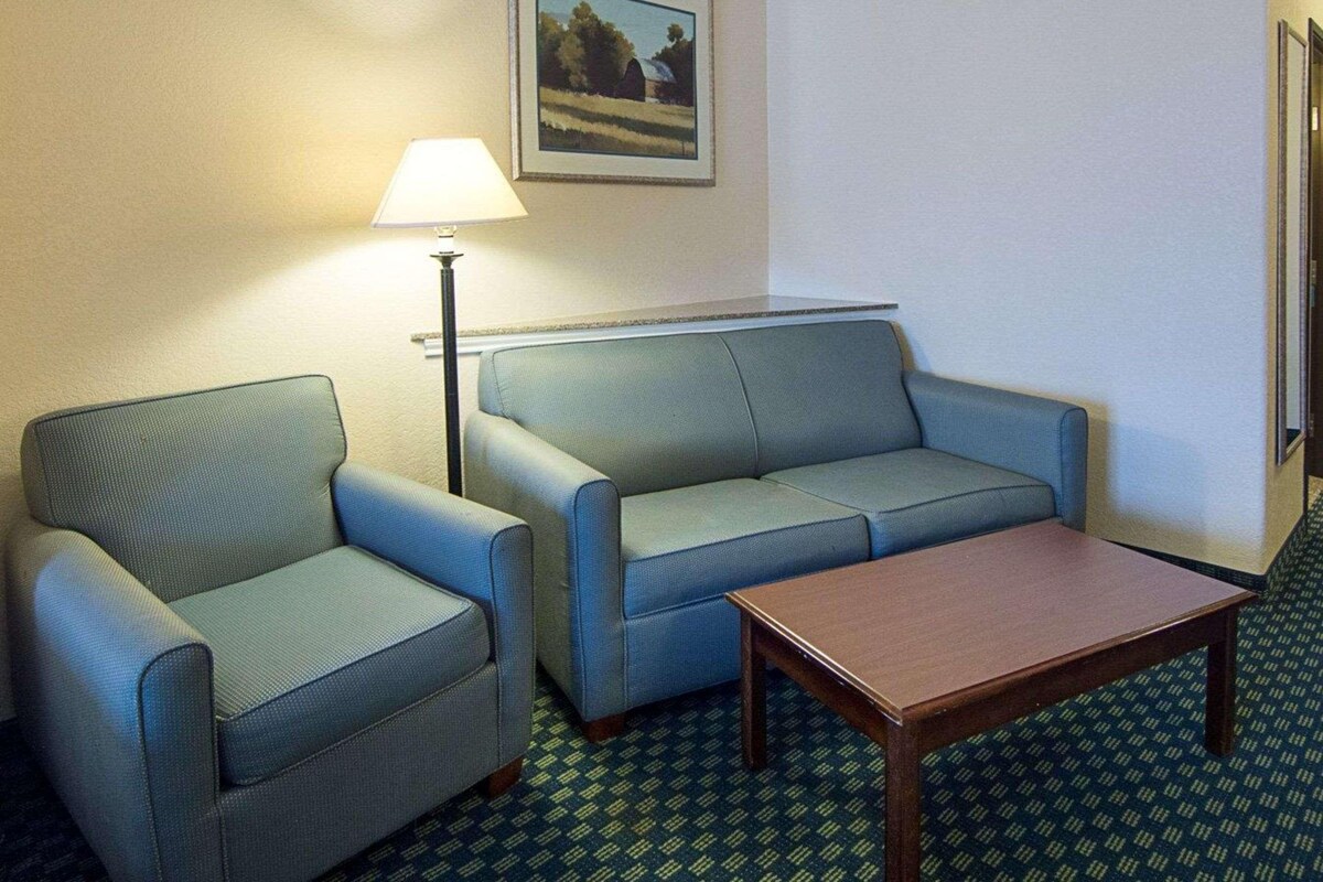 Une chambre d’hôtel avec un canapé bleu, un fauteuil plus petit, une table basse en bois et une lampe.