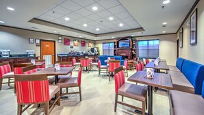 Un comedor de hotel con diversas opciones de asientos, incluyendo cabinas y mesas, una estación de café y un televisor.