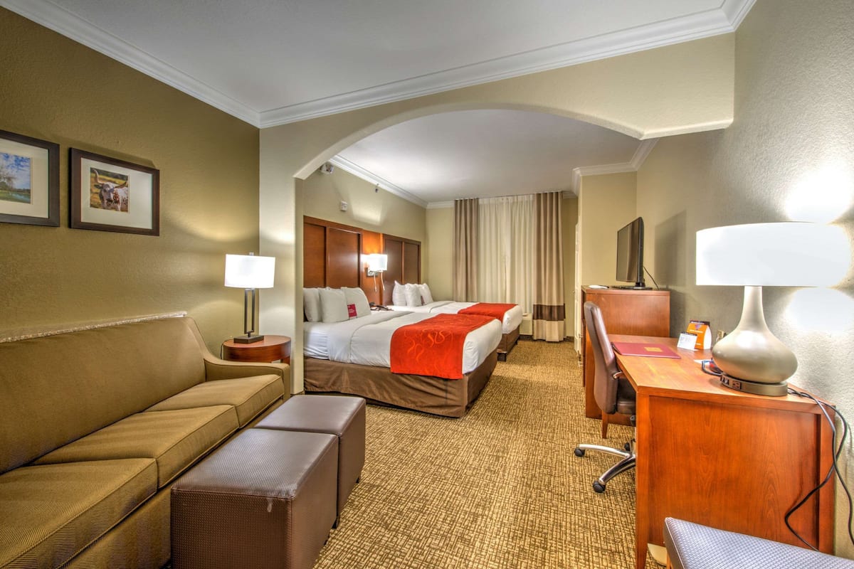 Une chambre d’hôtel avec un canapé, un bureau, un lit recouvert d’une couverture rouge, une lampe, une chaise et un téléviseur.