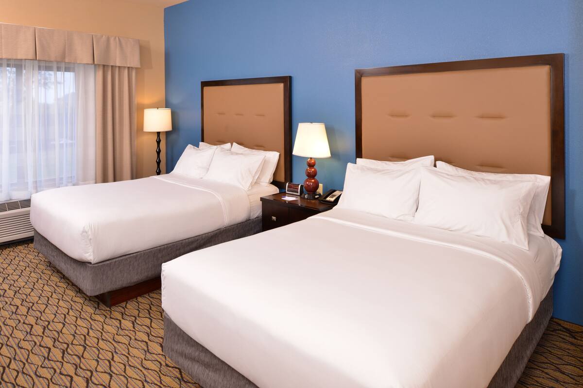 A hotel room with two beds, a nightstand with lamps, and a window with curtains.