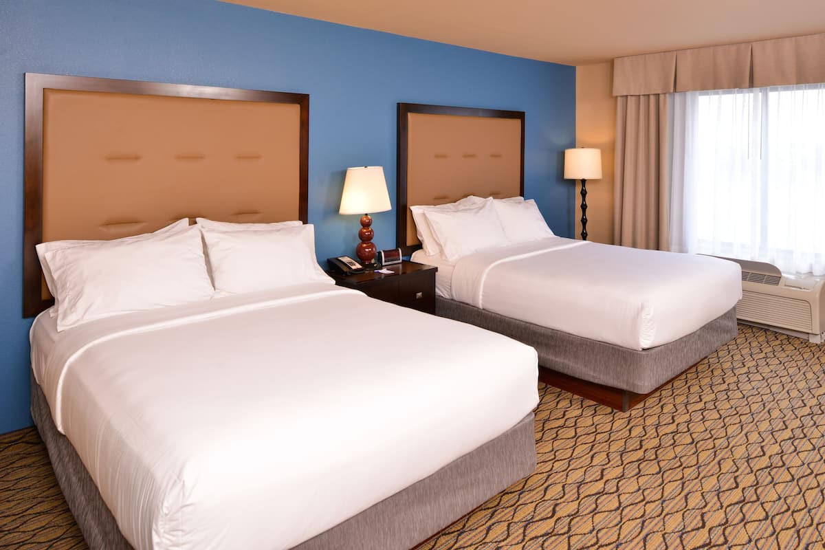 A hotel room with two beds, a nightstand with a lamp, and a window with curtains.