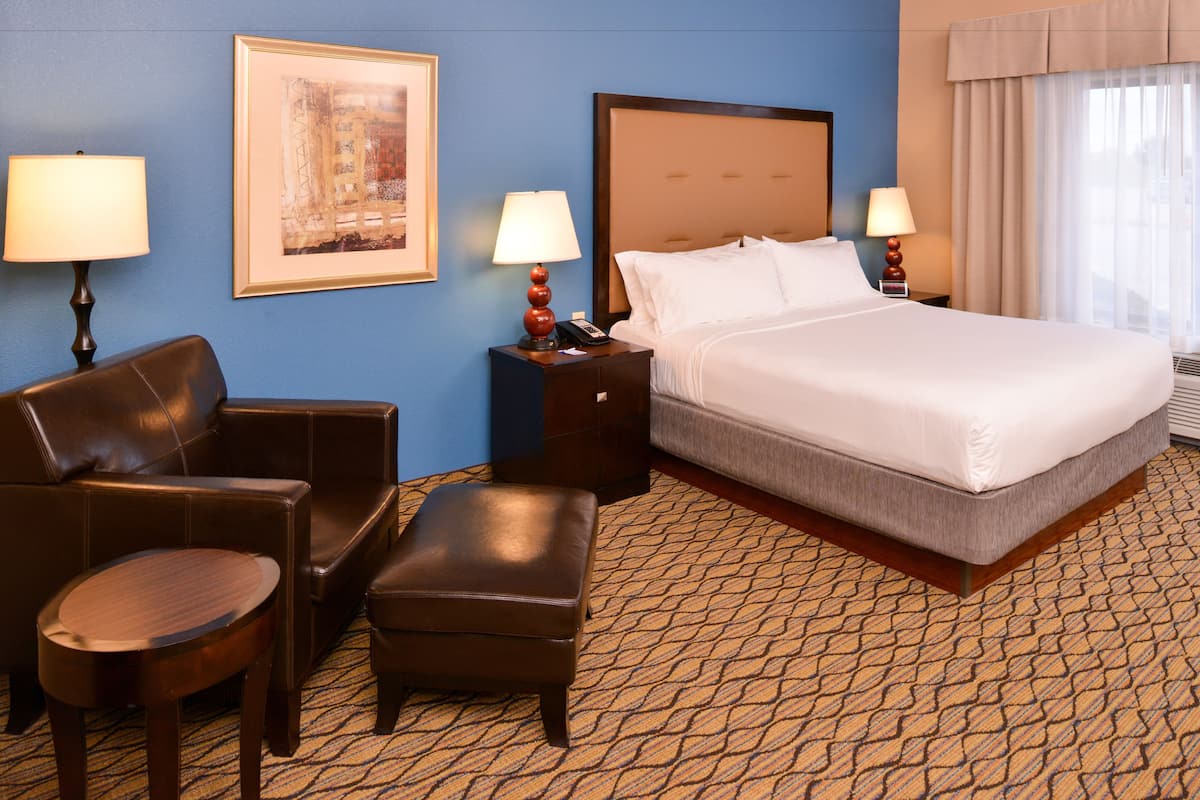 A hotel room with a large bed, two nightstands, a desk, a chair, and a sofa.
