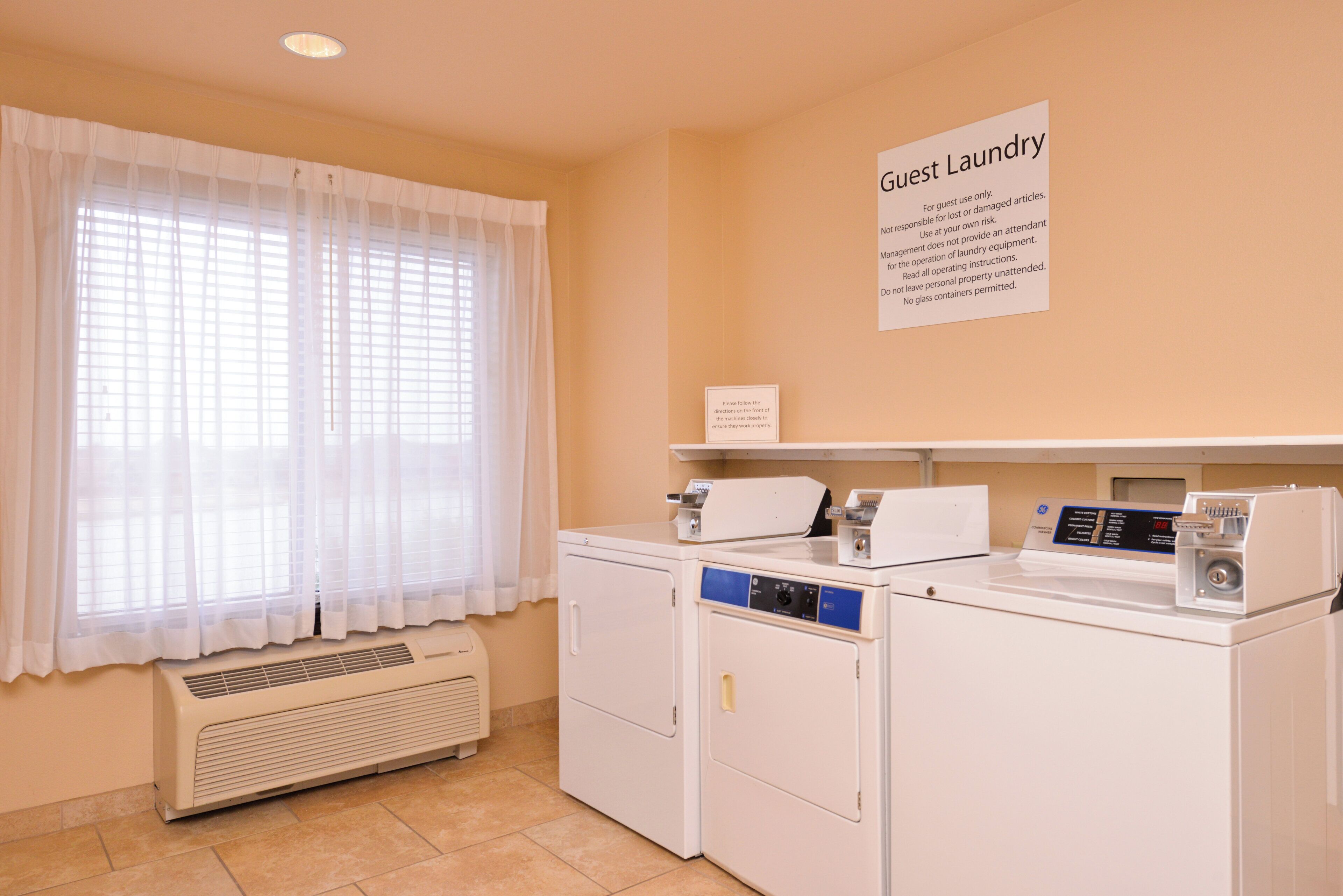 Un espace buanderie avec un panneau indiquant qu’il est réservé à l’usage des clients, un lave-linge à chargement frontal, un sèche-linge et une unité de ventilation.
