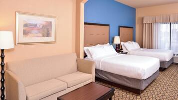 A hotel room with a sofa, two beds, a small table, and a painting on the wall.