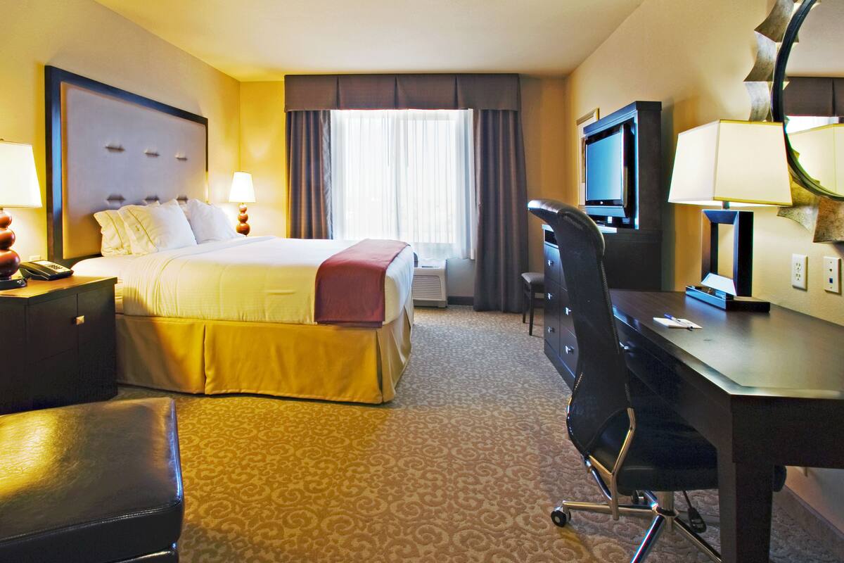 A hotel room with a bed, desk, chair, TV, and a lamp.