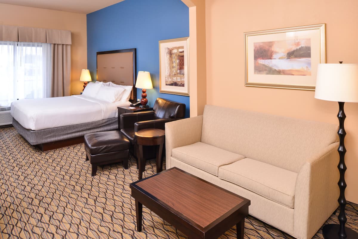 A hotel room with a bed, a sofa, a coffee table, a desk with a lamp, and two framed pictures on the wall.