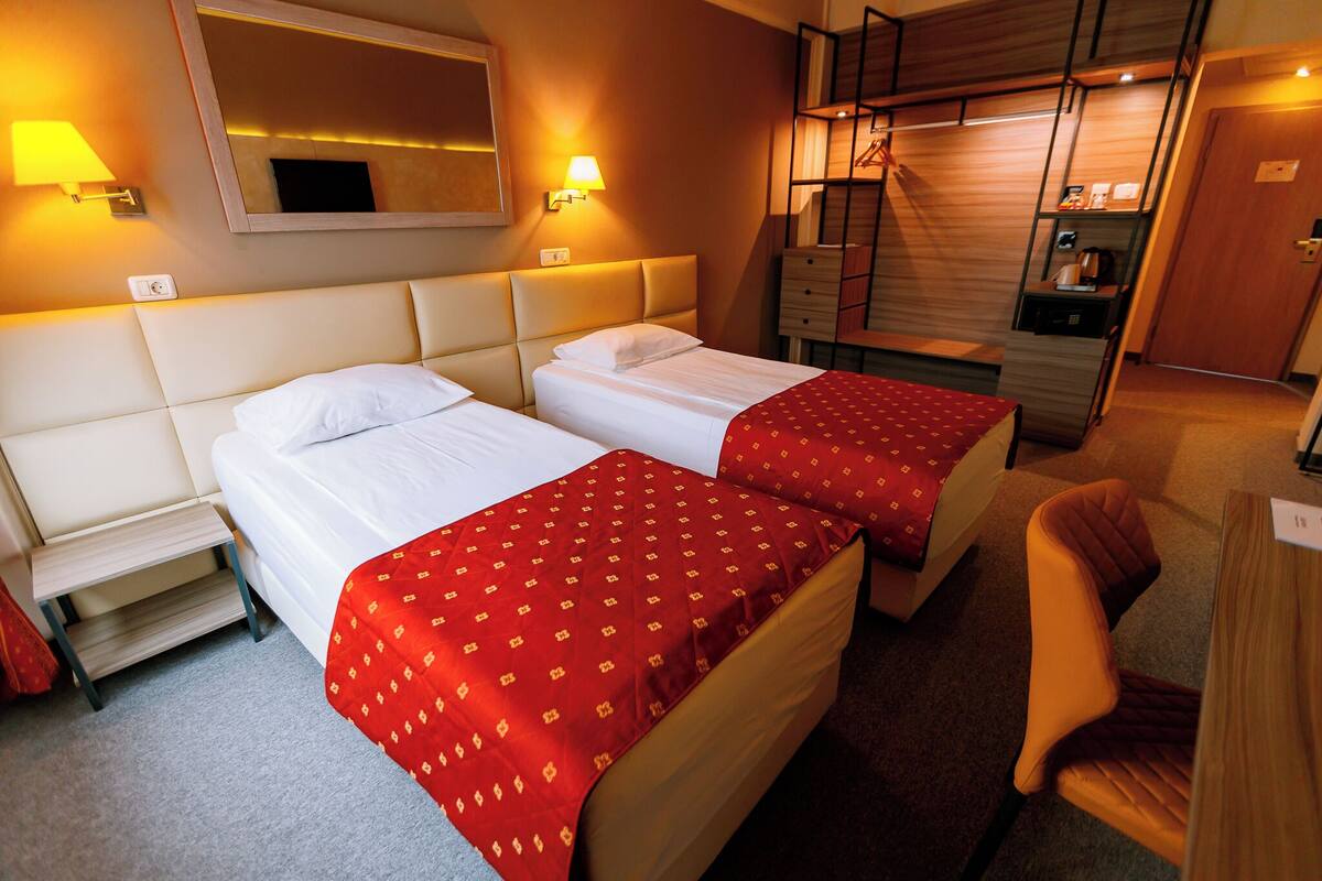 A hotel room with two beds, a desk, a chair, a mirror, and a wardrobe.