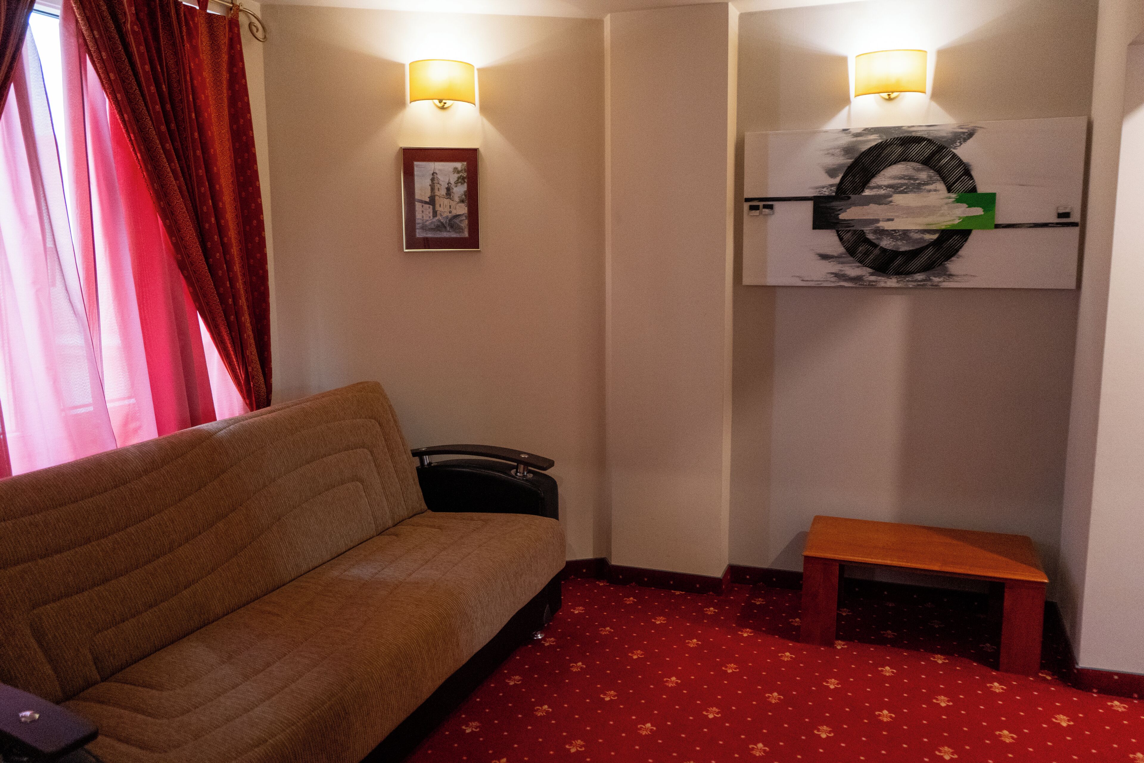 Une pièce comprenant un canapé, une petite table, une lampe fixée au mur et un tableau encadré.