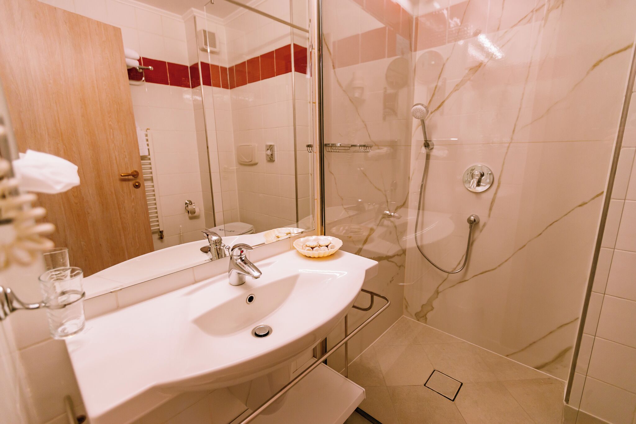 A bathroom with a white sink, a glass shower enclosure, and a marble-tiled shower wall.