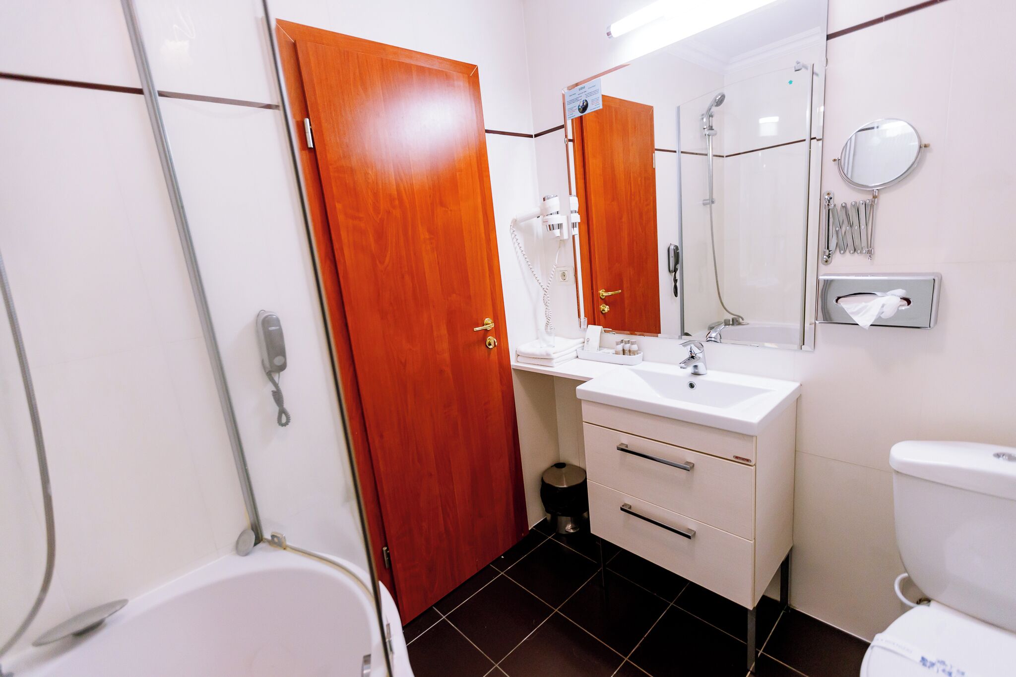 Ein Badezimmer mit Holztür, Waschbecken, Spiegel, Dusche und Toilette.
