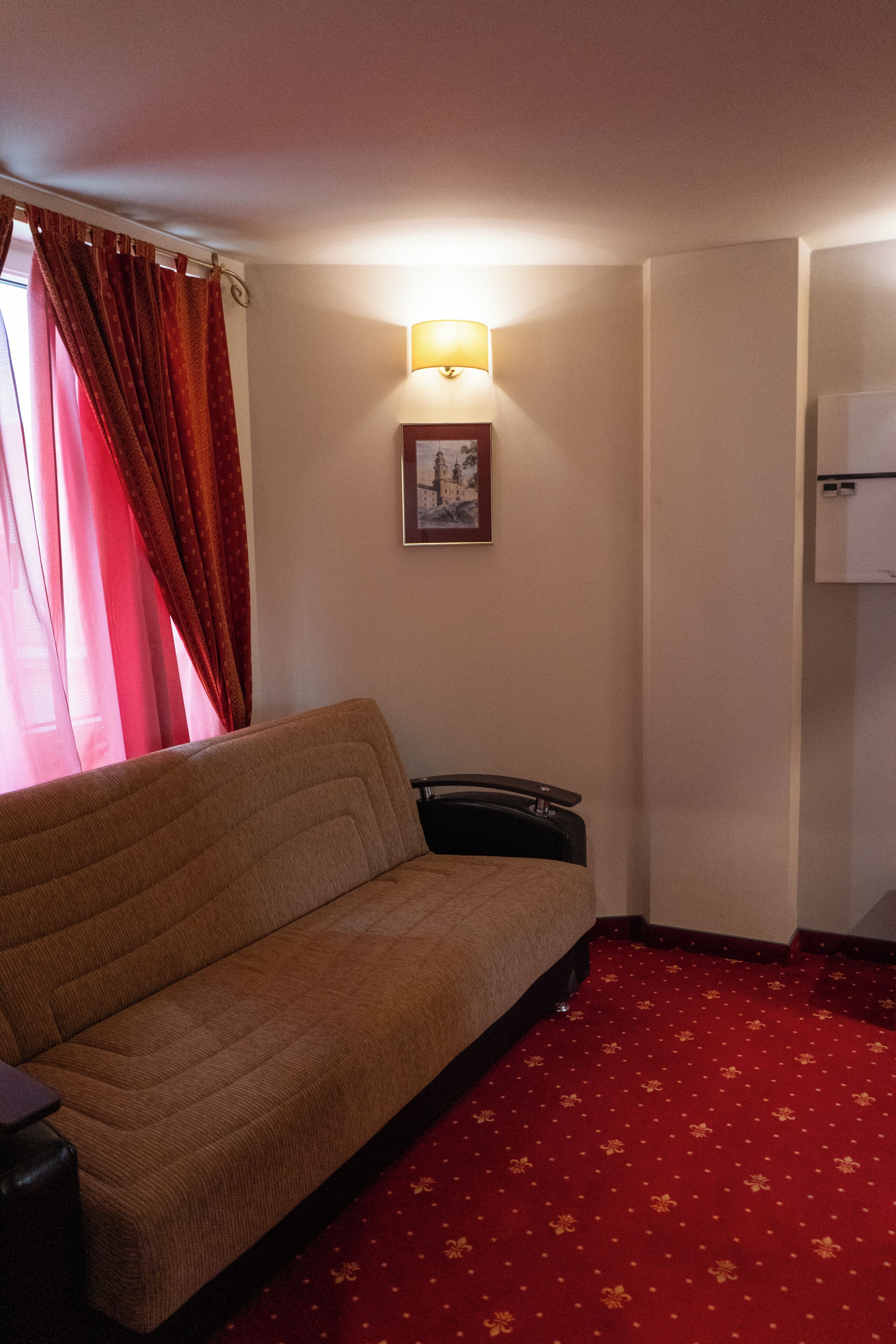 A room with a sofa, a red carpet, a wall-mounted lamp, and a framed picture.