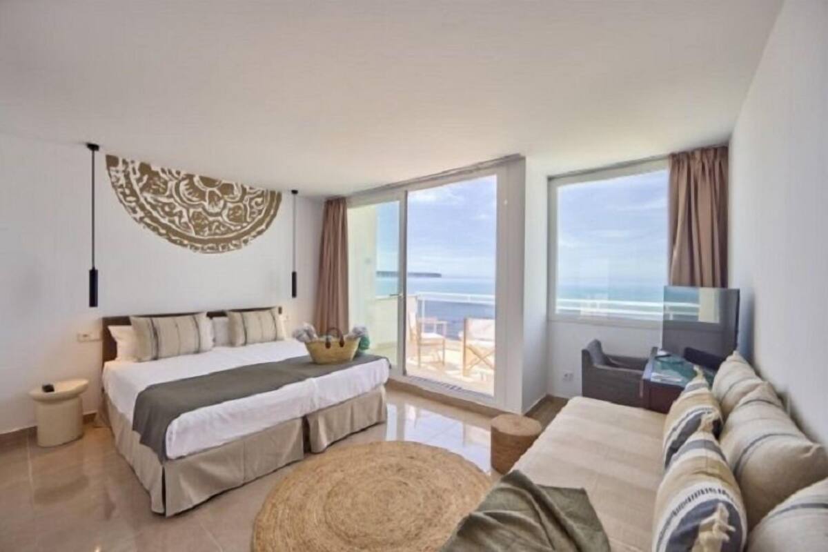 Ein modernes Schlafzimmer mit Bett, einer Couch, einem Fernseher und einem Balkon mit Meerblick.