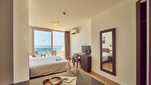Une chambre d’hôtel avec un lit, un bureau et une grande fenêtre donnant sur la mer.