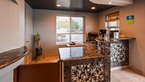 A reception area with a marble counter, a plant, a window with a view of parked cars, and a sign on the wall. - Downtown Phoenix Hotel (Phoenix)