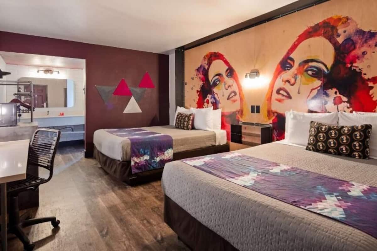 A hotel room with two beds, a desk, and a bathroom visible in the background.