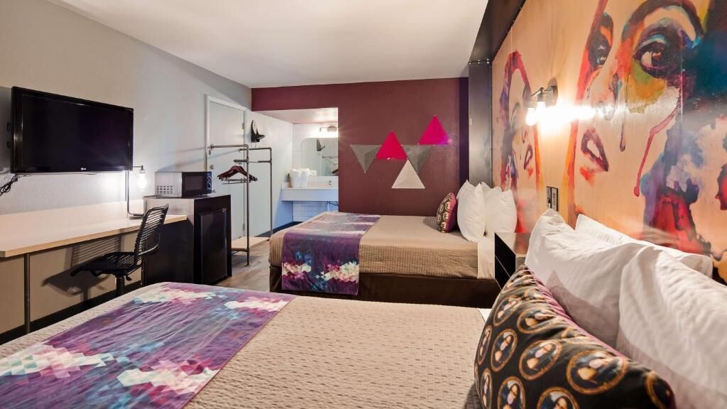 A hotel room with two beds, a desk, a TV, and a bathroom visible through an open door.