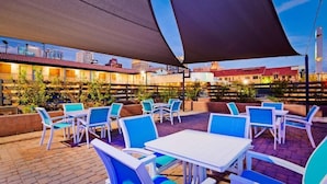 An outdoor patio area with white tables and blue chairs, surrounded by a brick wall and plants. - Downtown Phoenix Hotel (Phoenix)