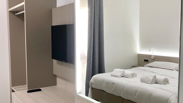 A modern hotel room with a large bed, a TV mounted on the wall, a desk with a chair, and a wardrobe. - Roy Hotel (Silea)