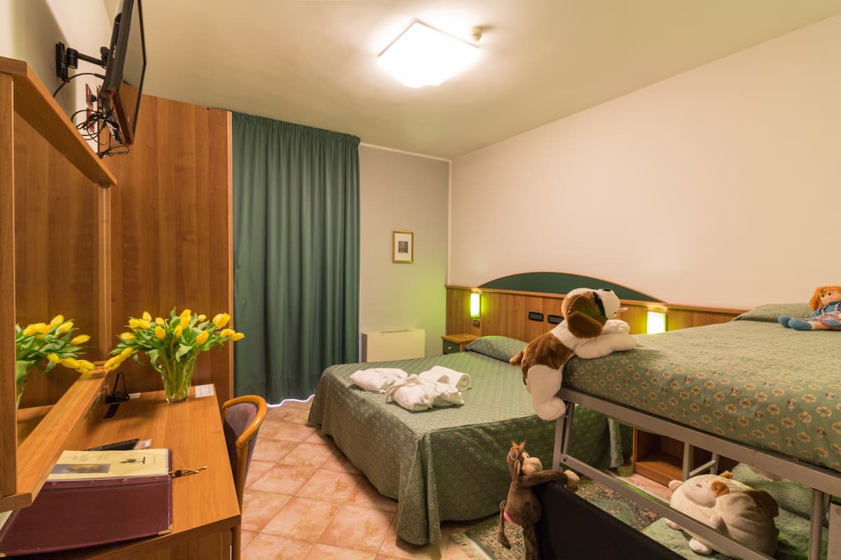 Habitación de hotel con un escritorio de madera, dos camas, un televisor y una pequeña mesa con flores.