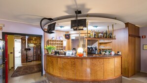 A hotel reception area with a wooden counter, a coffee machine, and a variety of bottles on shelves. - Roy Hotel (Silea)