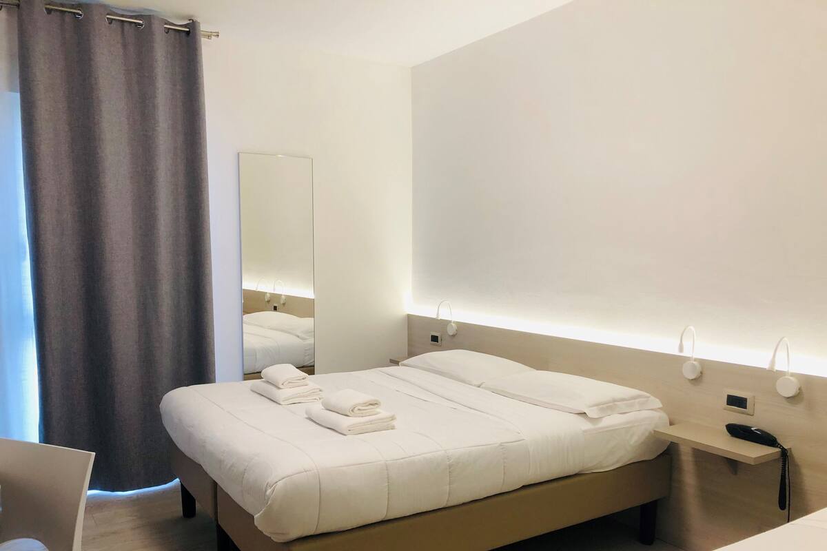 Una habitación de hotel moderna con una cama grande, mesitas de noche, un espejo y un teléfono junto a la cama.