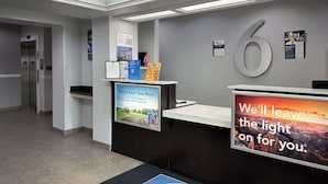 A hotel reception area with a digital screen displaying a booking message, a large number '6' on the wall, and a doormat with the hotel's logo. - Motel 6 Mission, TX (Mission)