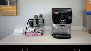 A coffee station with a Folgers coffee maker, disposable cups, and a sign indicating coffee hours from 6:00 am to 10:00 am. - Motel 6 Mission, TX (Mission)