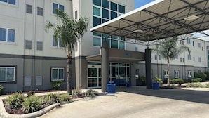 A modern motel with a covered entrance, large windows, and a palm tree in the foreground. - Motel 6 Mission, TX (Mission)