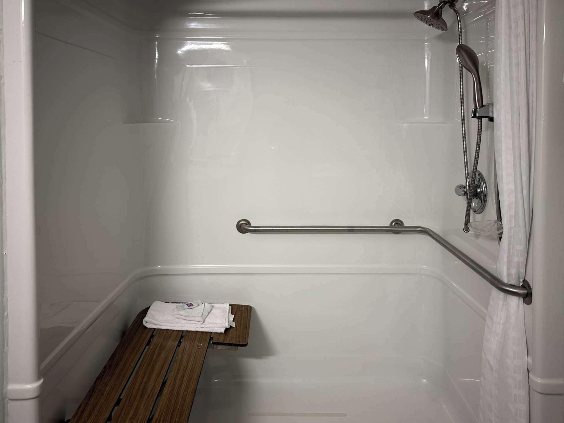 A bathroom with a shower, a grab bar, and a wooden bench.