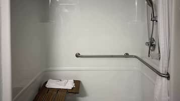 A bathroom with a shower, a grab bar, and a wooden bench.