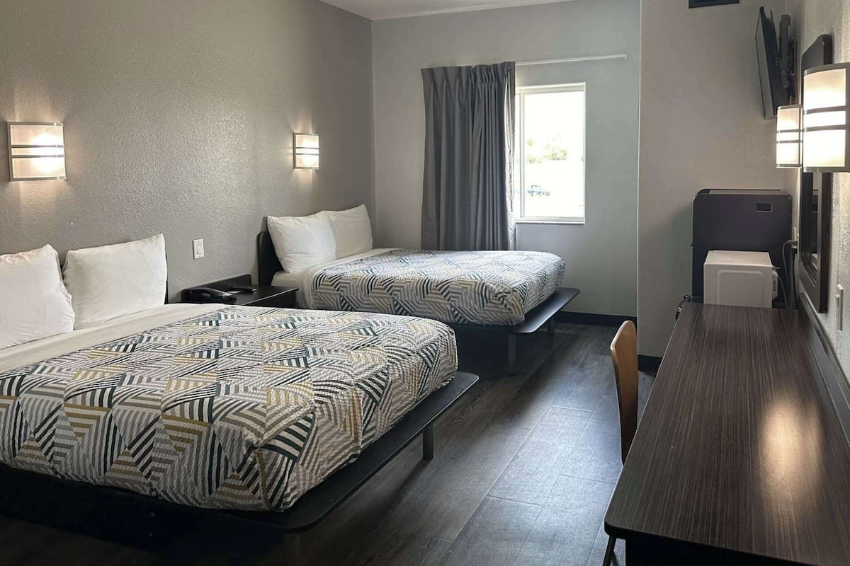 A hotel room with two beds, a desk, a chair, and a window with curtains.