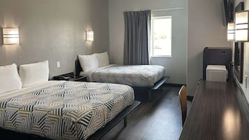 A hotel room with two beds, a desk, a chair, and a window with curtains.