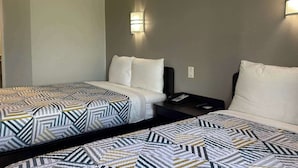 A hotel room with two beds, each with patterned bedding, a bedside table with a phone, and wall-mounted lighting. - Motel 6 Mission, TX (Mission)