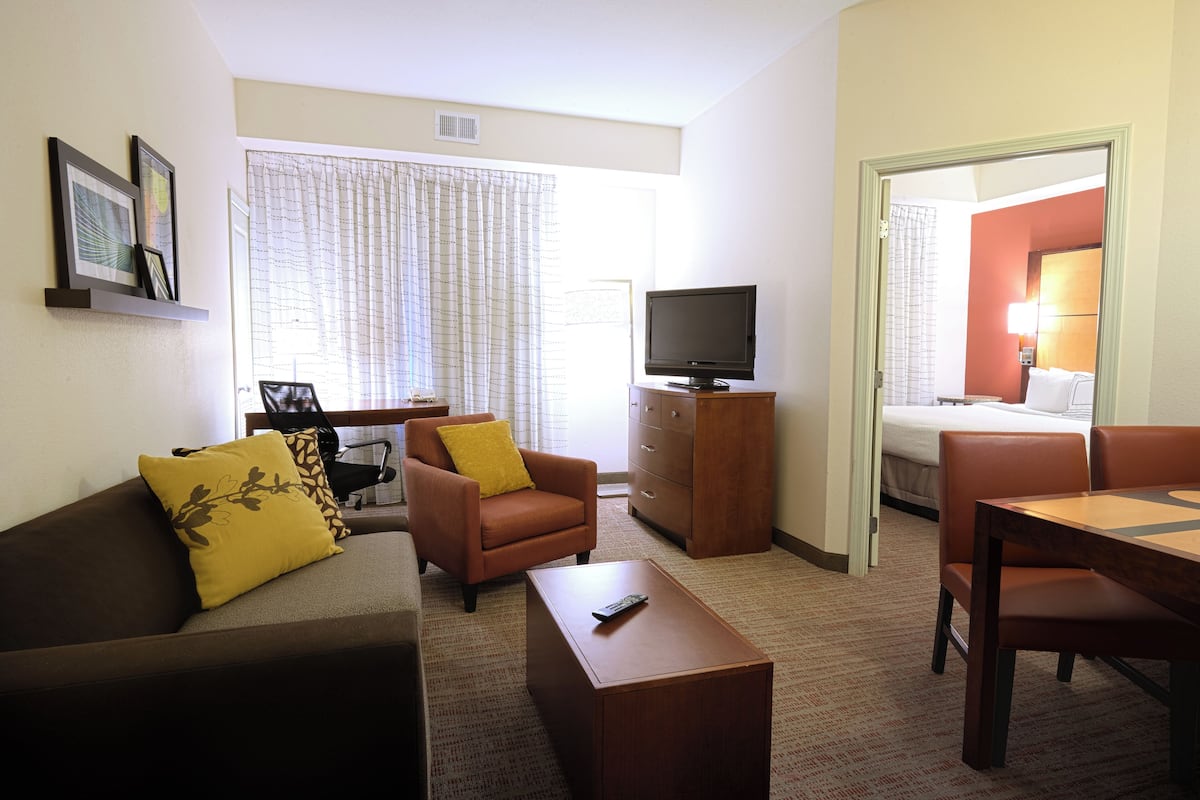 Ein Hotelzimmer mit Sofa, Sessel, Couchtisch, Fernseher und Esstisch.