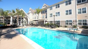 Une piscine à l’eau d’un bleu limpide, entourée d’une clôture et jouxtant un immeuble à plusieurs étages doté de balcons.