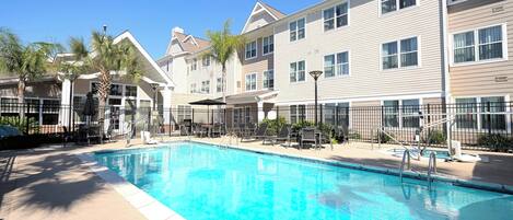 A swimming pool with a clear blue water, surrounded by a fence, and adjacent to a multi-story building with balconies.