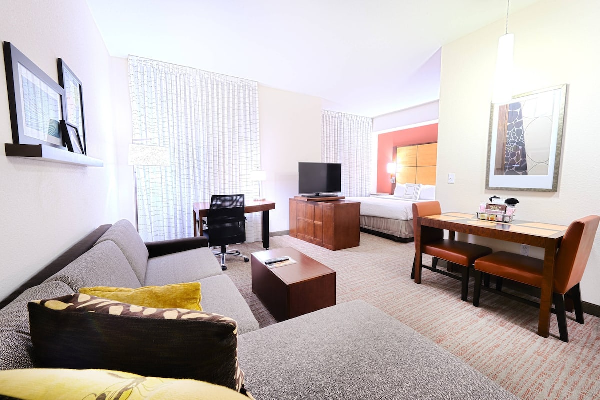 Ein Hotelzimmer mit einer Couch, einem Couchtisch, einem Fernseher, einem Schreibtisch mit Stuhl und einem Bett.