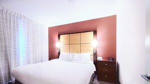 Une chambre d’hôtel avec un grand lit, une tête de lit en bois, deux tables de chevet avec des lampes et une petite table de nuit avec un téléphone.