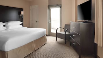 A hotel room with a large bed, a TV on a dresser, a chair, and a door leading to a balcony.